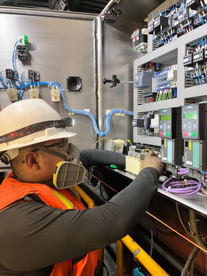 Services Electrician wearing safety gear adjusting wires on a control panel in Callao, Perú.