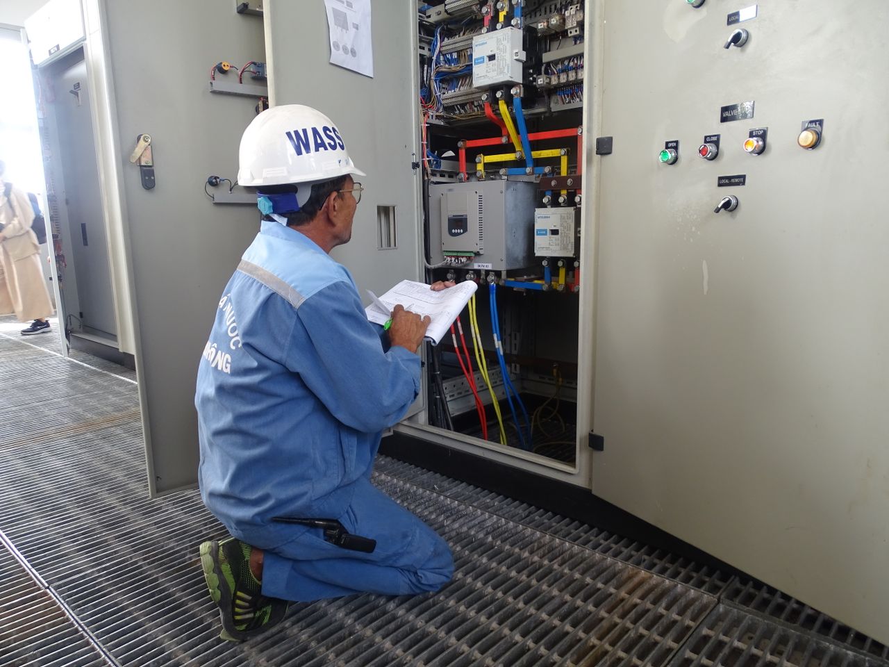 Services Engineer in uniform inspecting an electrical control panel in an industrial setting.